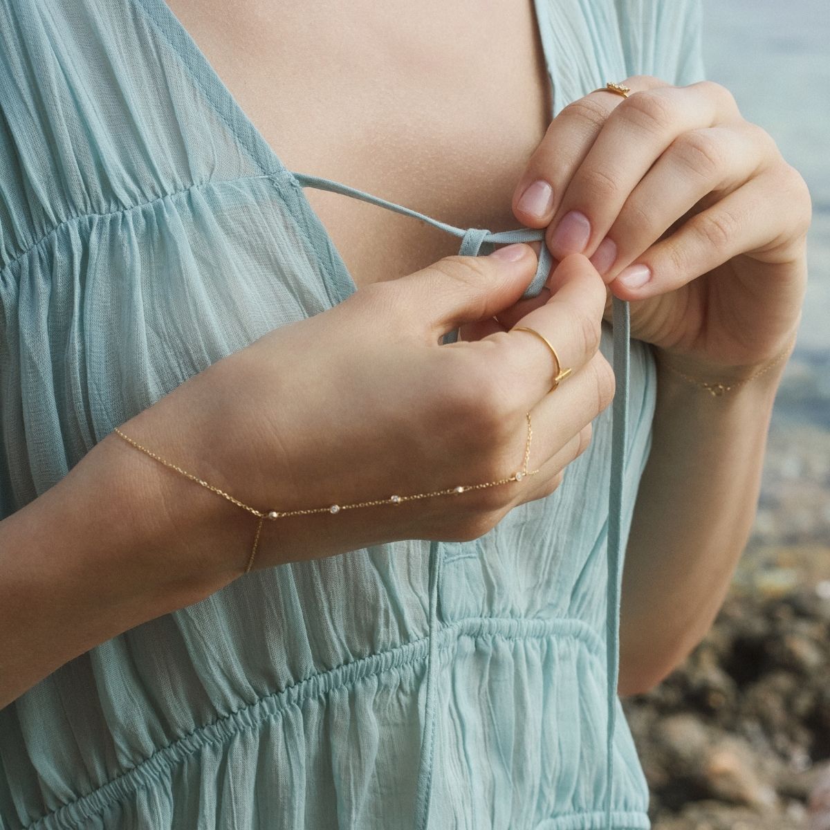 Close-up of a woman's hands wearing a light blue shirt styled with a delicate hand chain diamond bracelet.