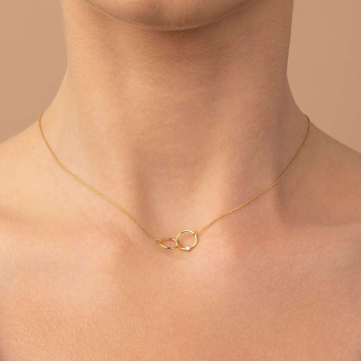 Model wearing the 14k yellow gold interlocking double circle necklace close to the collarbone.