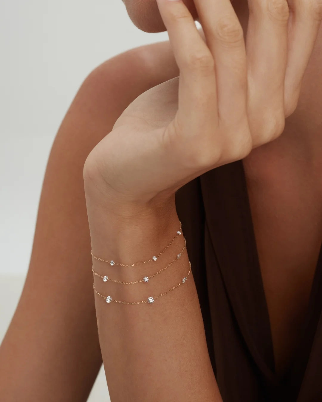 Close-up of a wrist wearing three delicate bracelets with small drilled diamonds on a neutral background