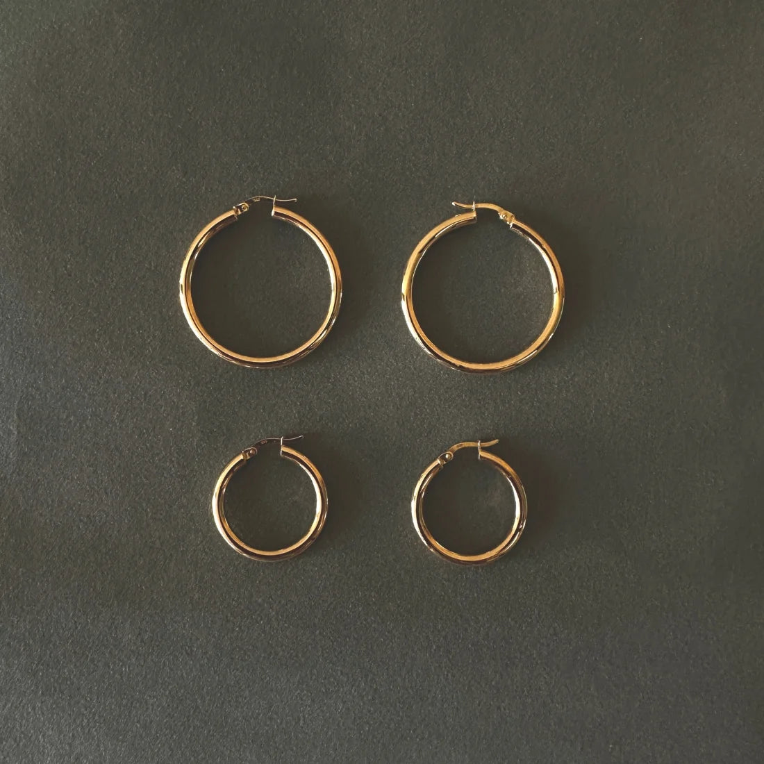 Four 14k gold hoop earrings of two different sizes placed on a dark gray background - ENEA