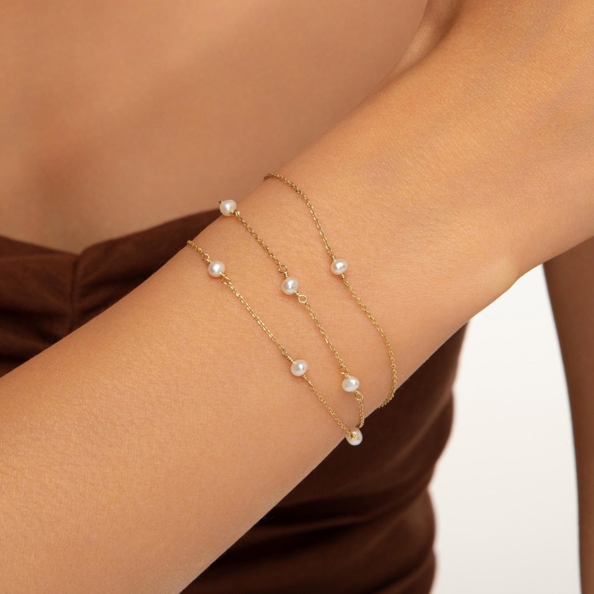 Model stacking the 14k yellow gold multi pearl bracelet with other delicate gold chains on the wrist.

