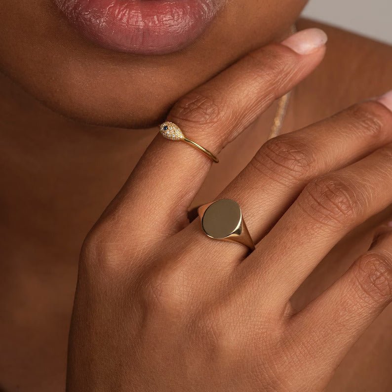 Close-up of a woman’s hand adorned with the yellow gold oval signet ring, paired with other delicate gold jewelry, showcasing a sleek and personalized aesthetic
