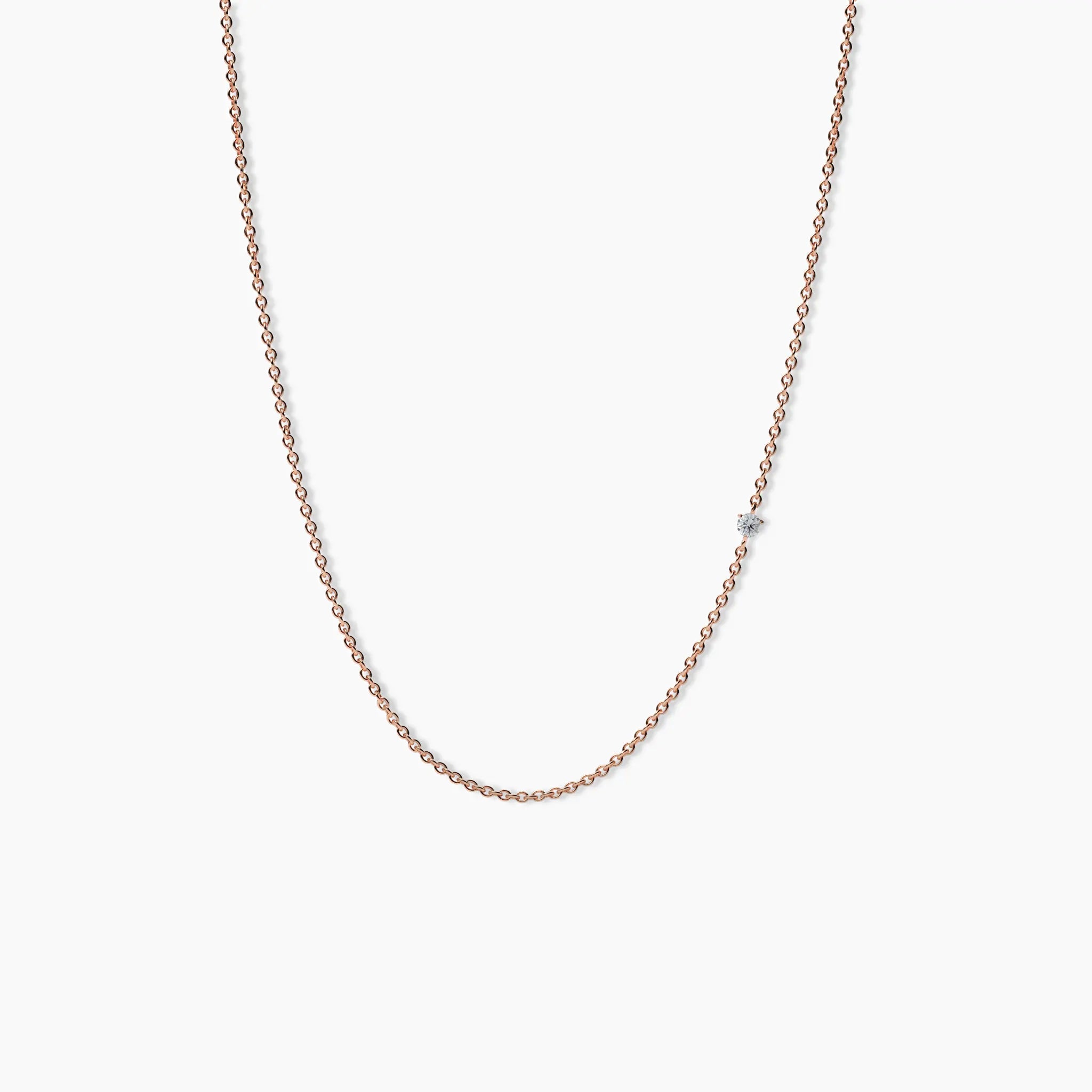 Delicate rose gold necklace with a single small diamond set along a thin chain, displayed on a white background.
