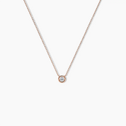Delicate rose gold necklace featuring a round bezel-set diamond pendant on a fine chain, shown on a white background.
