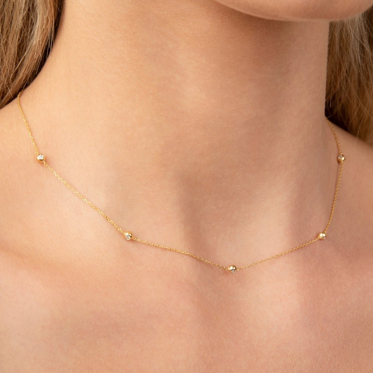Close-up view of 14k yellow gold necklace with five round-cut diamonds spaced across the neckline.