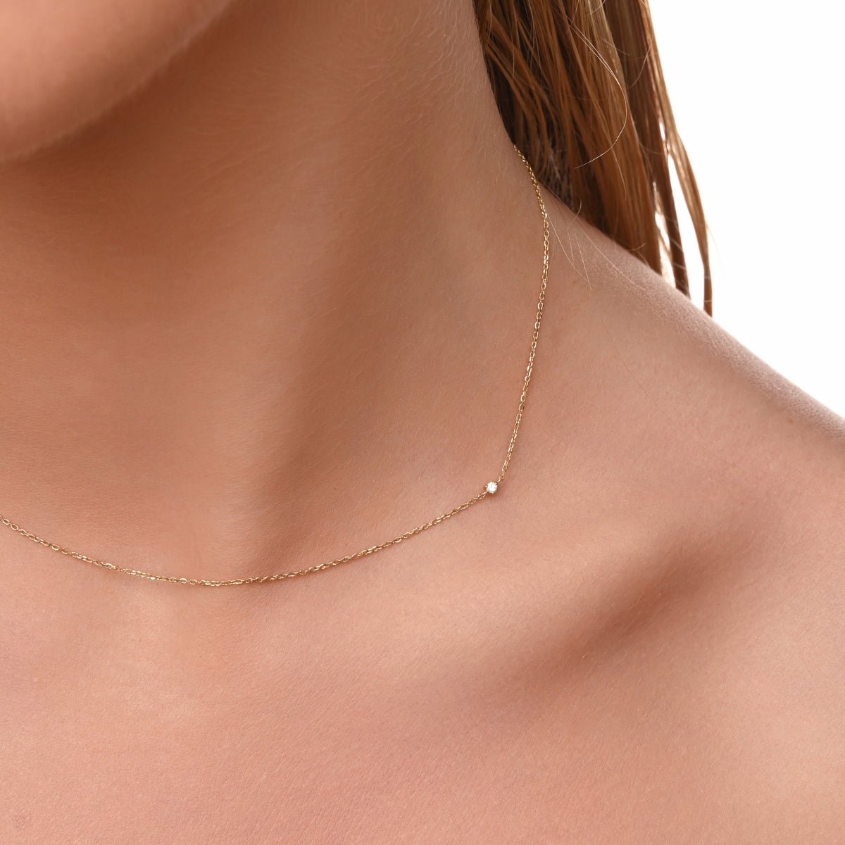 Close-up of a woman wearing a minimalist 14k gold necklace featuring a single tiny diamond off-center on a fine chain.
