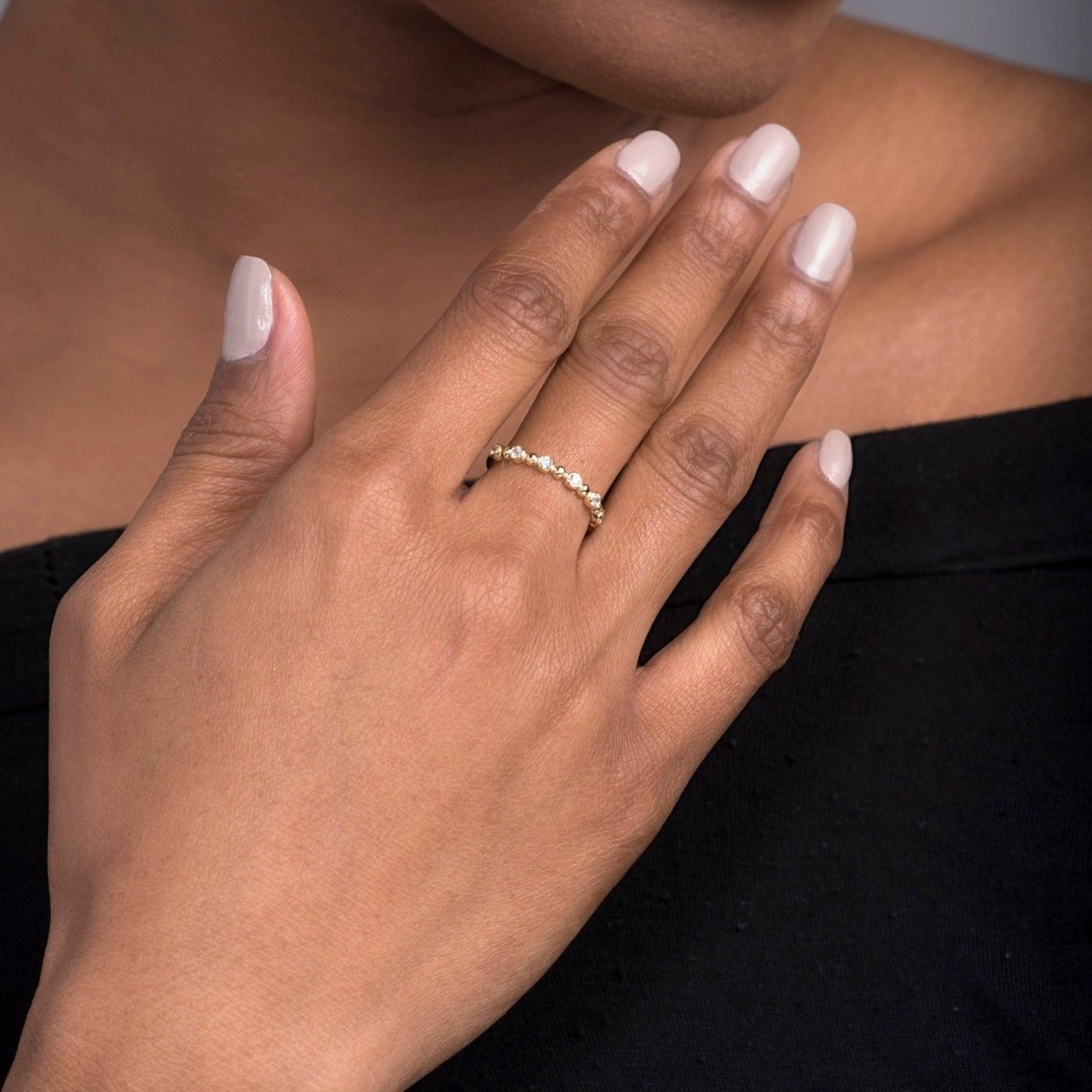 A woman’s hand styled with a 14k yellow gold beaded diamond ring, showing its delicate gold spheres and bezel-set diamonds. A subtle and sophisticated jewelry statement.