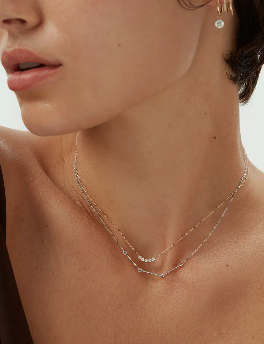 Close-up view of a woman wearing a 14k white gold Iris Necklace with bar and loop detail, layered with a diamond dot necklace.