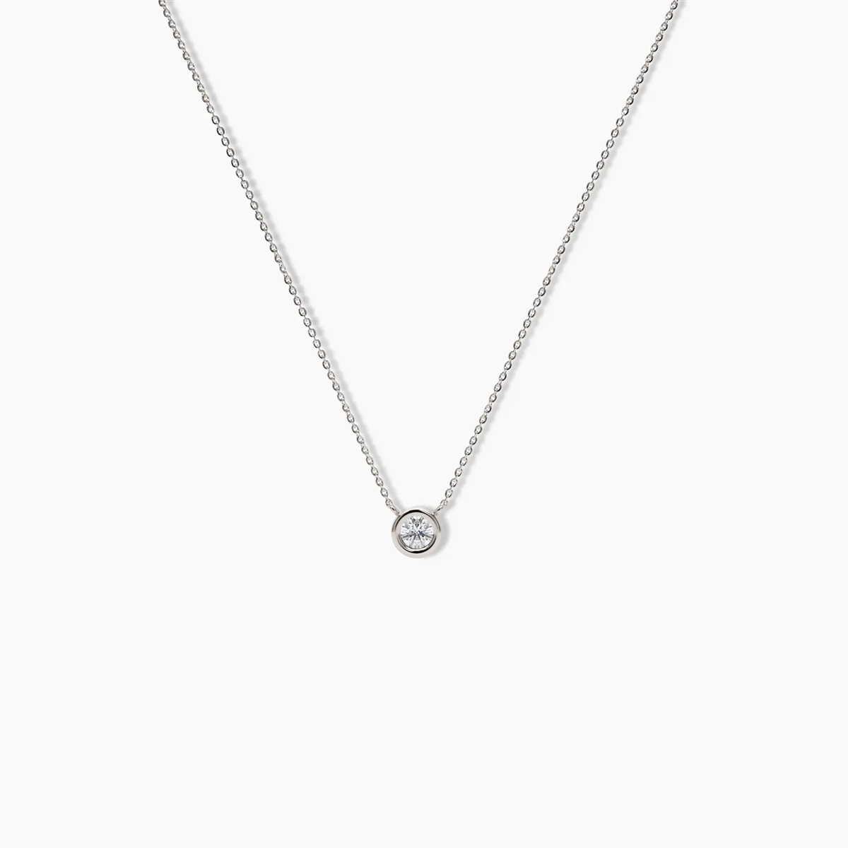 Single white gold necklace with a round bezel-set diamond pendant displayed against a white background.
