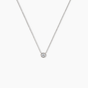 Single white gold necklace with a round bezel-set diamond pendant displayed against a white background.
