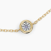 Macro shot of a brilliant-cut diamond encased in a gold bezel, centered on a fine chain for a refined finish.


