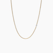 Close-up of a yellow gold necklace with a single small diamond set along a delicate chain, shown on a clean white background.

