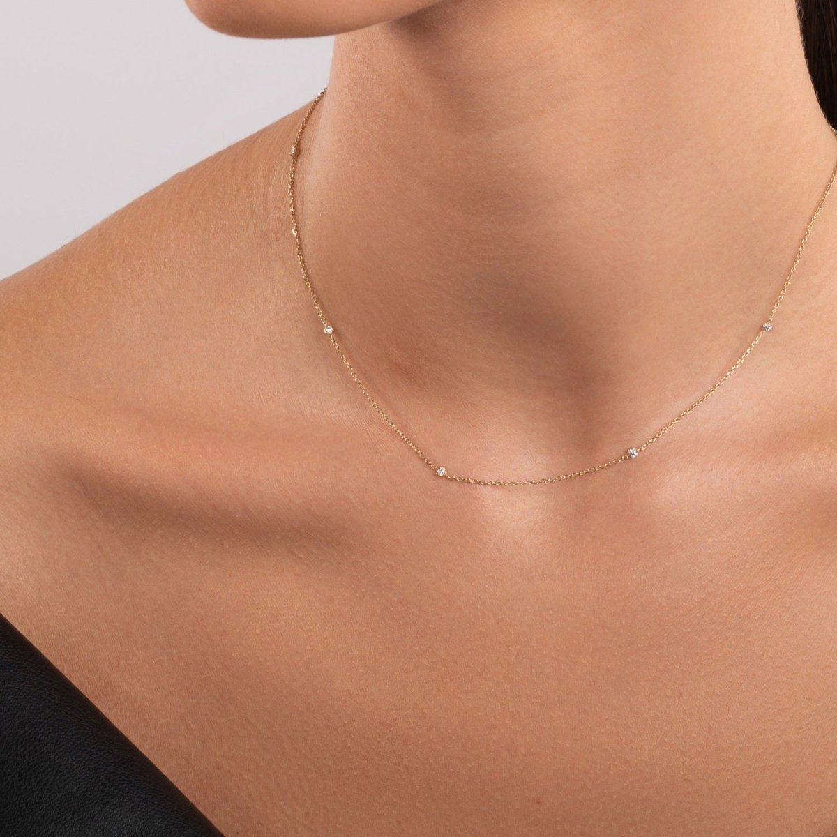 Close-up of a woman wearing a delicate 14k gold necklace with five evenly spaced round diamonds on a fine chain
