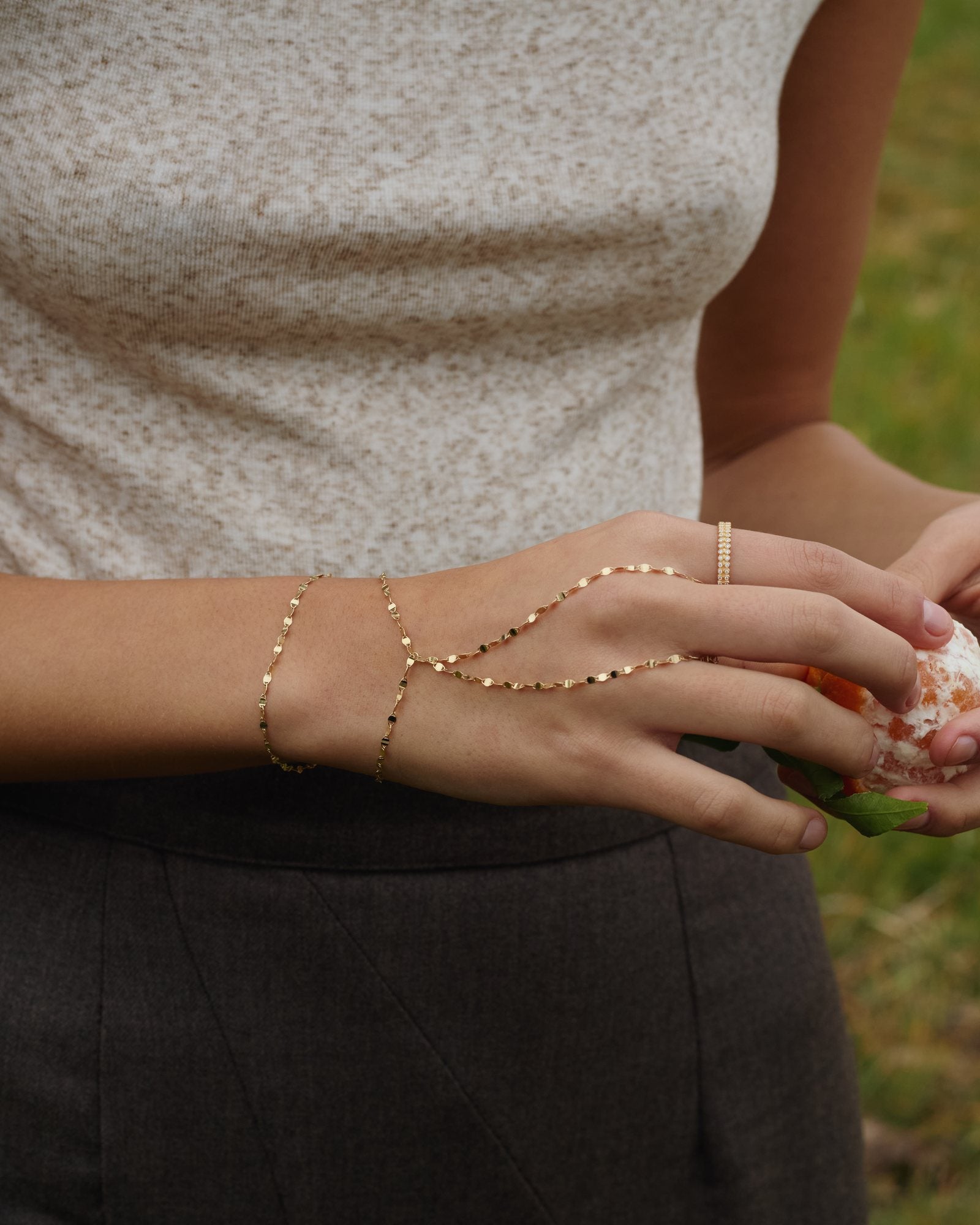 Hand wearing a gold diamond station hand chain and rings, holding a stone
