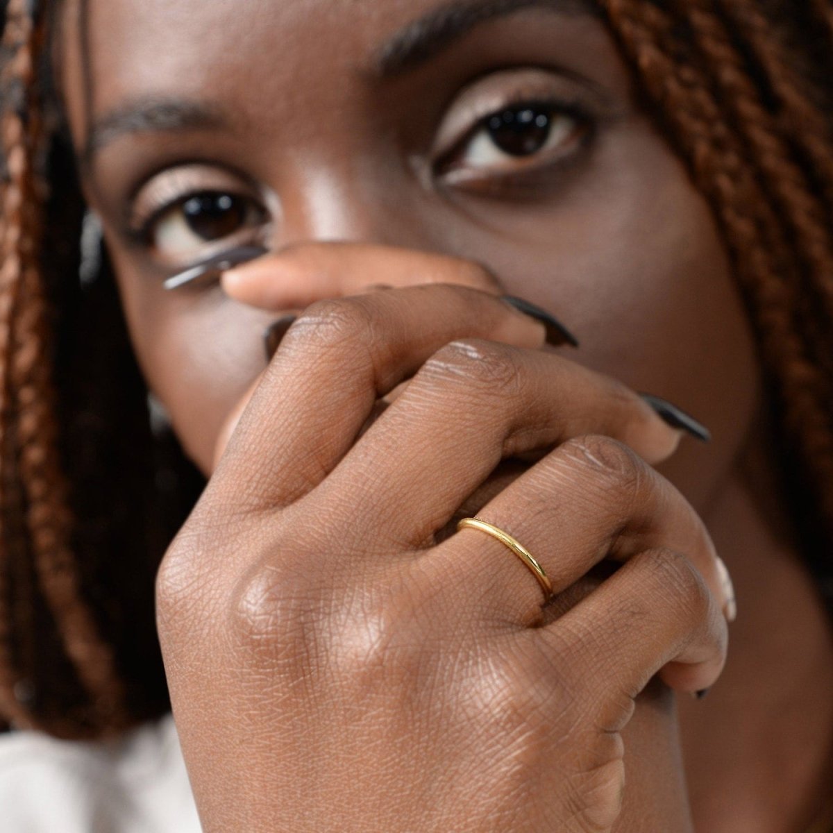 A woman wearing a 14k yellow gold thin band, gently resting her hand near her face. The ring’s delicate design adds a subtle touch of elegance.
