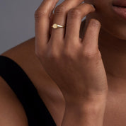A woman’s hand styled with a 14k yellow gold oval signet ring, highlighting its sleek, polished surface and refined elegance.