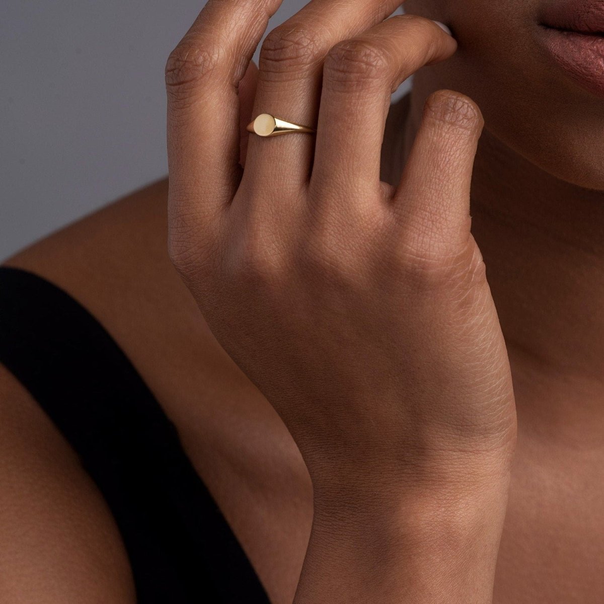 A woman’s hand styled with a 14k yellow gold oval signet ring, highlighting its sleek, polished surface and refined elegance.
