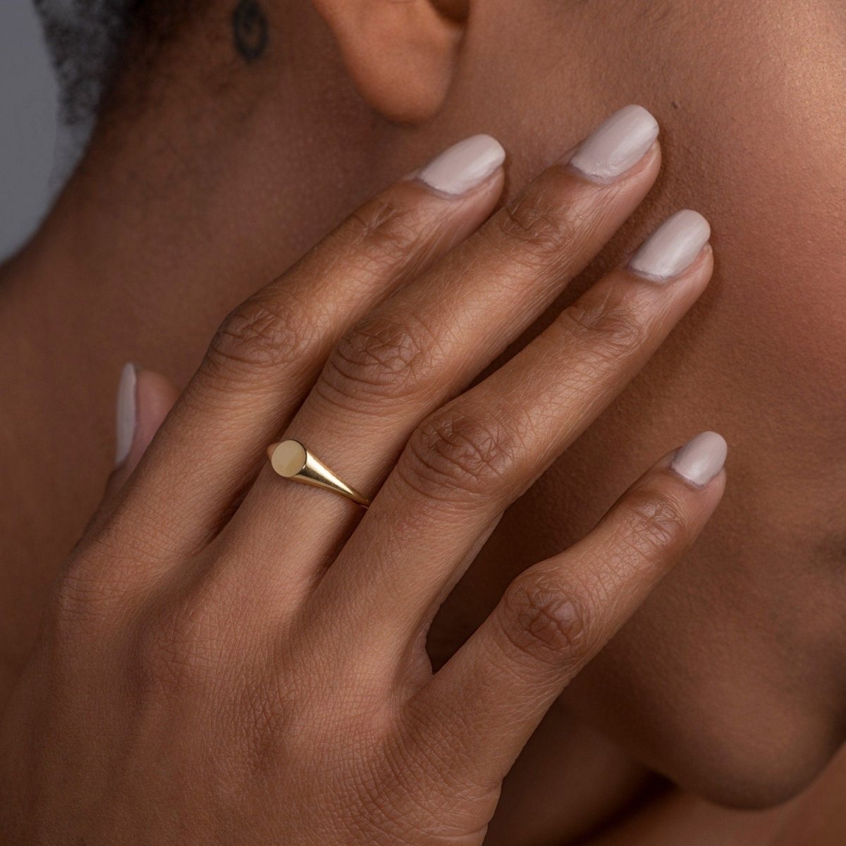 A woman touching her face while wearing a 14k yellow gold oval signet ring, emphasizing its classic design and sophisticated presence.