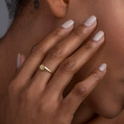 A woman touching her face while wearing a 14k yellow gold oval signet ring, emphasizing its classic design and sophisticated presence.