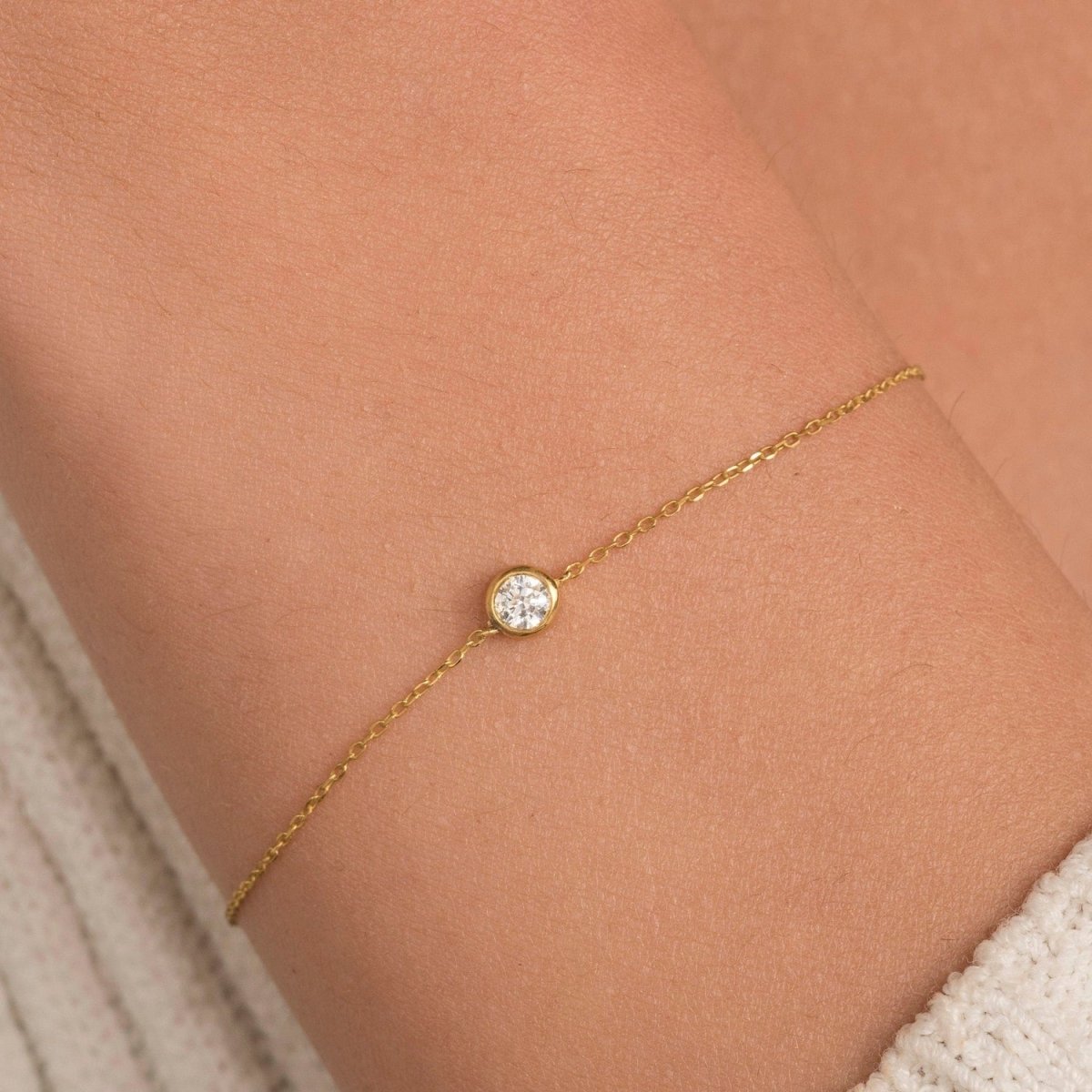 Close-up of a dainty diamond bracelet in 14k yellow gold, worn on wrist to highlight the bezel-set centerpiece under natural lighting.

