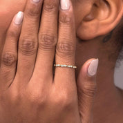 A close-up of a woman wearing a 14k rose gold twisted diamond eternity band on her index finger, highlighting its elegant twisted shape and sparkling diamonds.