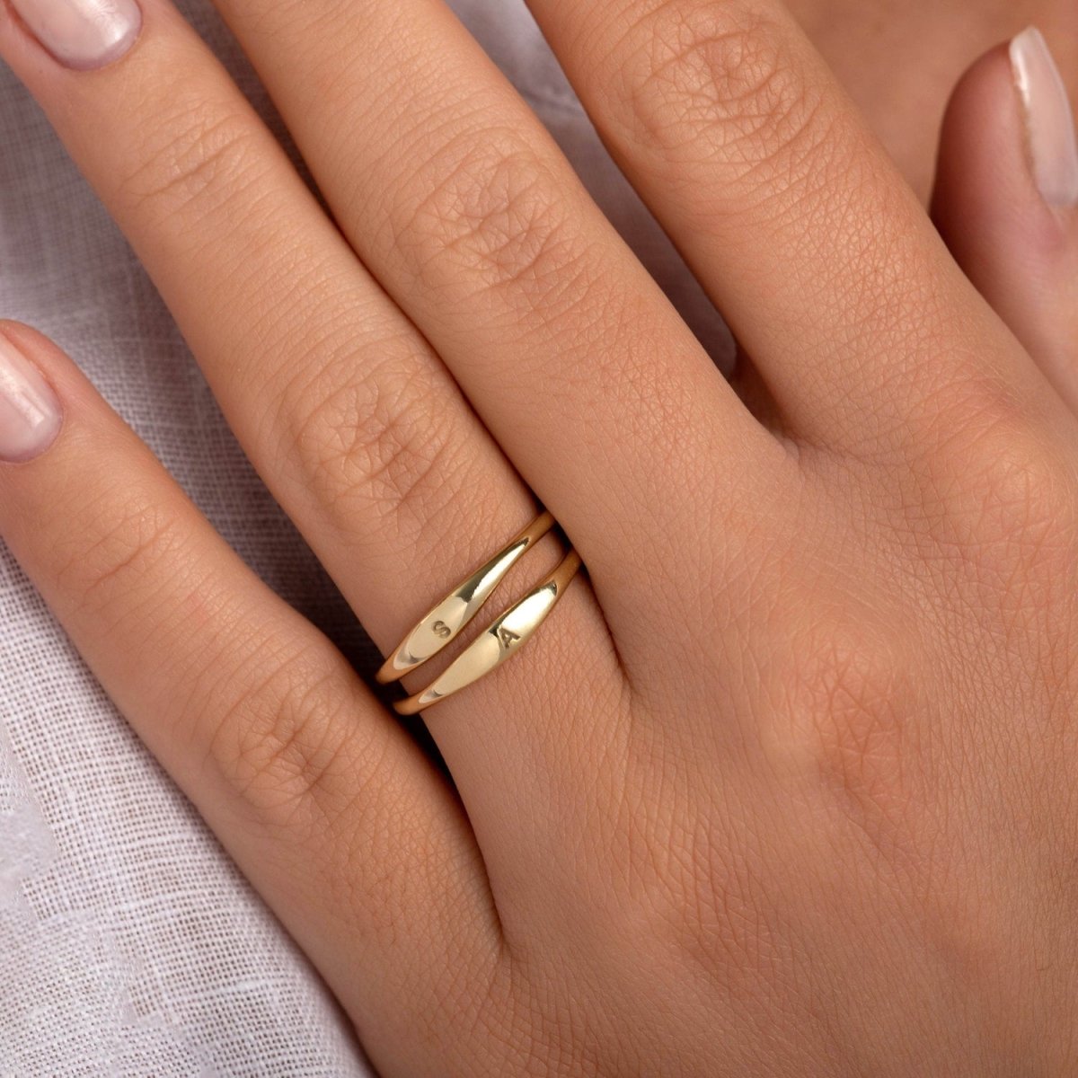 model wearing the yellow gold tiny signet ring stacked with other dainty gold bands, showcasing its versatility and elegant simplicity
