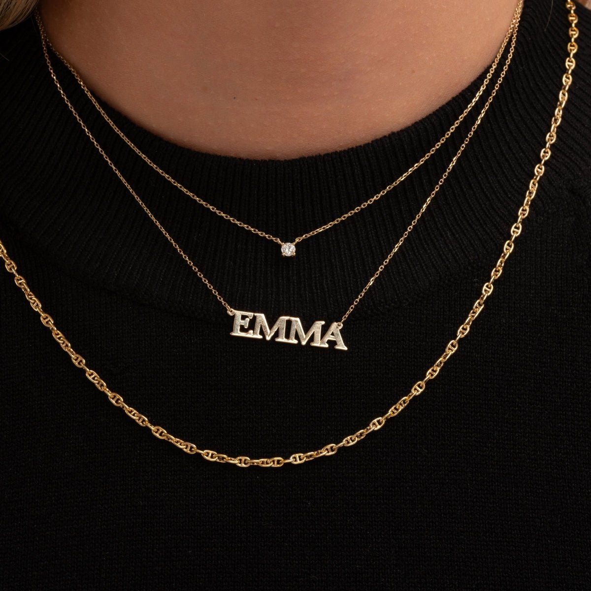 layered 14k gold necklaces on model wearing black top, featuring diamond solitaire and personalized name necklace EMMA
