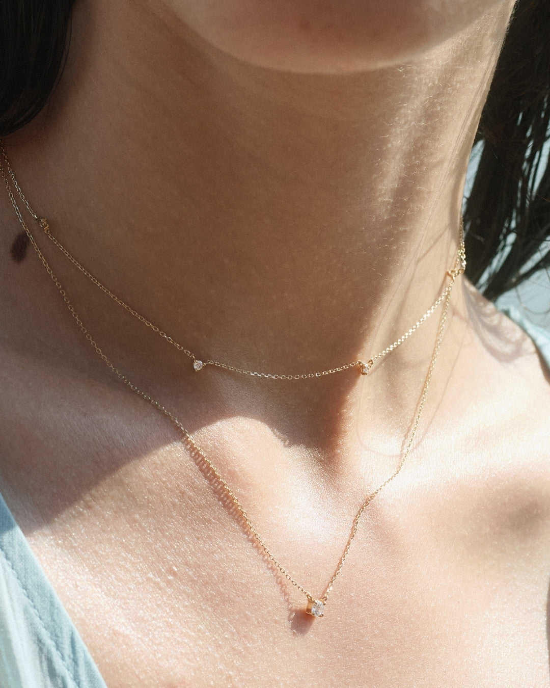 Close-up of a woman's neck styled with a delicate gold necklace with station diamonds layered with a longer gold chain necklace accented with a prong-set solitaire diamond.
