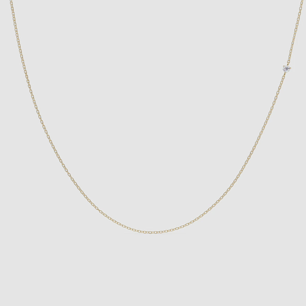 Close-up video of a delicate gold chain necklace with a single small diamond station. The necklace hangs gently against a white background, with soft lighting highlighting the sparkle of the diamond as the chain subtly sways.
