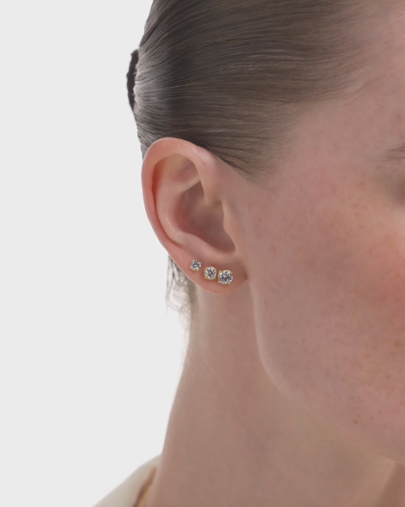 close-up video of a woman wearing the eclat grand diamond earring studs stacked in three different diamond sizes on one ear, and two slightly bigger diamond sizes stacked on the other ear against an off-white background