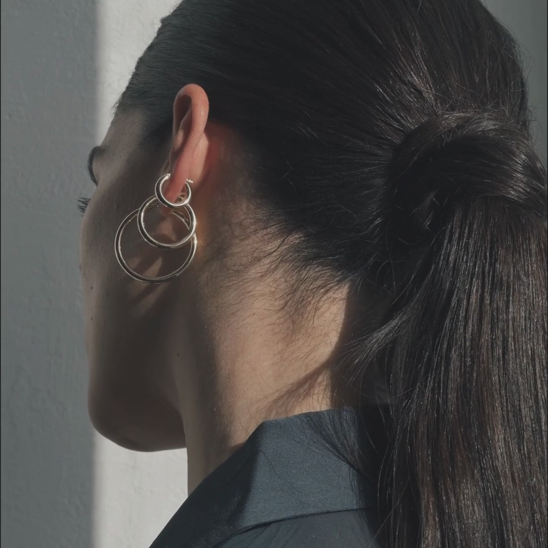 Close-up side video of a model wearing 3 gold hoop earrings with her hair pulled back in soft, natural light.
