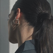 Close-up side video of a model wearing 3 gold hoop earrings with her hair pulled back in soft, natural light.