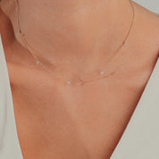 14k gold necklace with spaced round diamonds, shown worn close to the neck on a model, highlighting its barely-there shimmer and delicate floating design.
