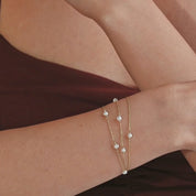 Close-up of 14k yellow gold bracelet with luminous white pearls styled on bare skin.