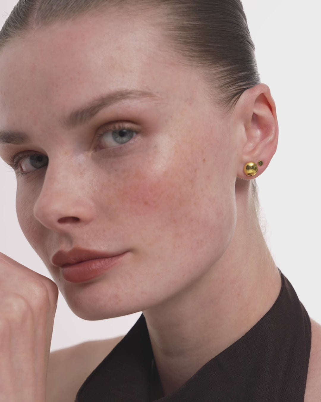 Video of a woman wearing the Diskos Disc Studs in 14k yellow gold, a small polished gold disc catching light as she turns. ENEA Studio
