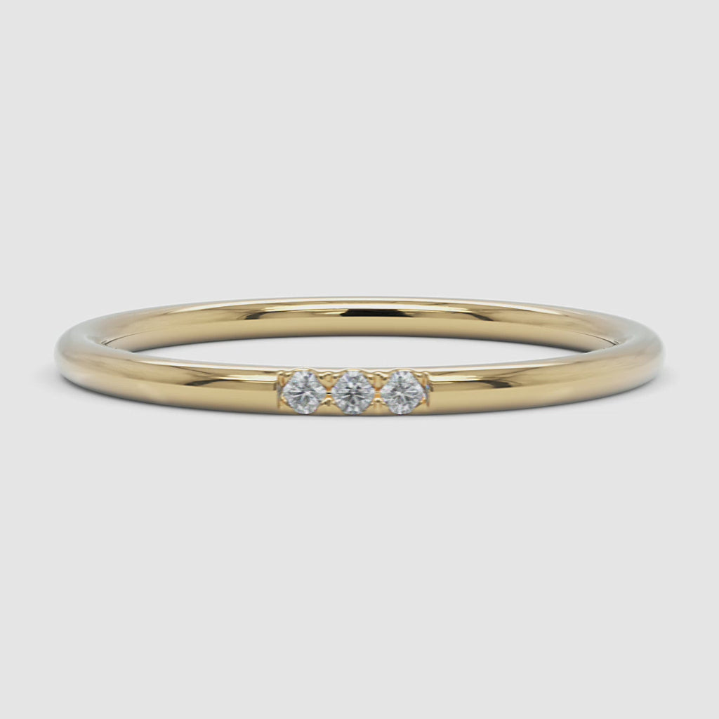 A 360-degree video of a 14k yellow gold slim diamond band, smoothly rotating to reveal its fine, polished band and three round diamonds set in a delicate arrangement.