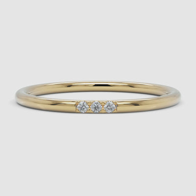 A 360-degree video of a 14k yellow gold slim diamond band, smoothly rotating to reveal its fine, polished band and three round diamonds set in a delicate arrangement.
