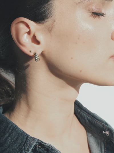 Model slowly turning to showcase 14k gold croissant hoops, emphasizing shine and texture in natural light.