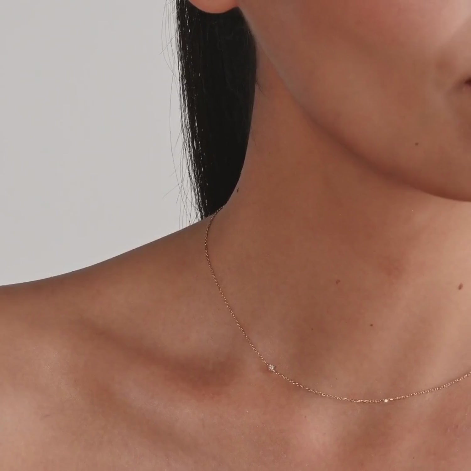 Close-up of a woman wearing a delicate 14k gold necklace with a single diamond set subtly off-center on a fine chain, captured mid-motion in a video.
