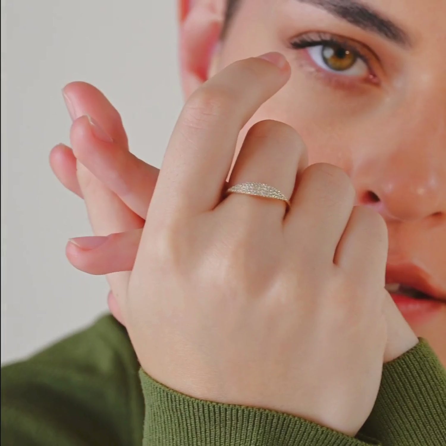 A video of a woman wearing a 14k yellow gold pavé diamond band, moving her hands to showcase the delicate sparkle of the pavé diamonds and the ring’s elegant curvature.
