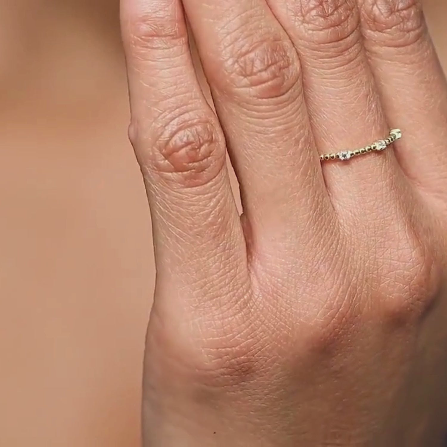 A close-up video of a woman wearing a 14k yellow gold diamond beaded ring, moving her hand to reveal the intricate gold bead details and prong-set diamonds. The ring catches the light, showcasing its elegant sparkle.