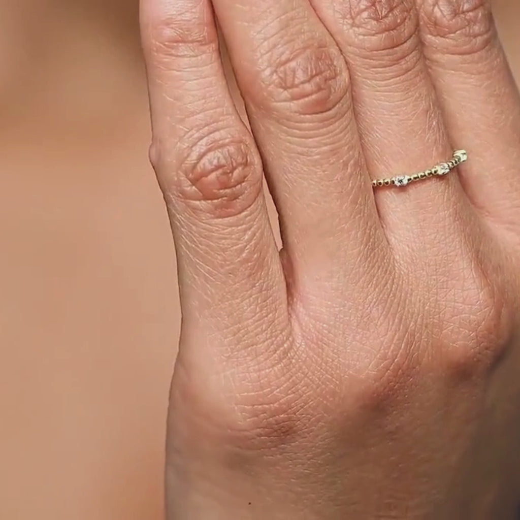 A close-up video of a woman wearing a 14k yellow gold diamond beaded ring, moving her hand to reveal the intricate gold bead details and prong-set diamonds. The ring catches the light, showcasing its elegant sparkle.