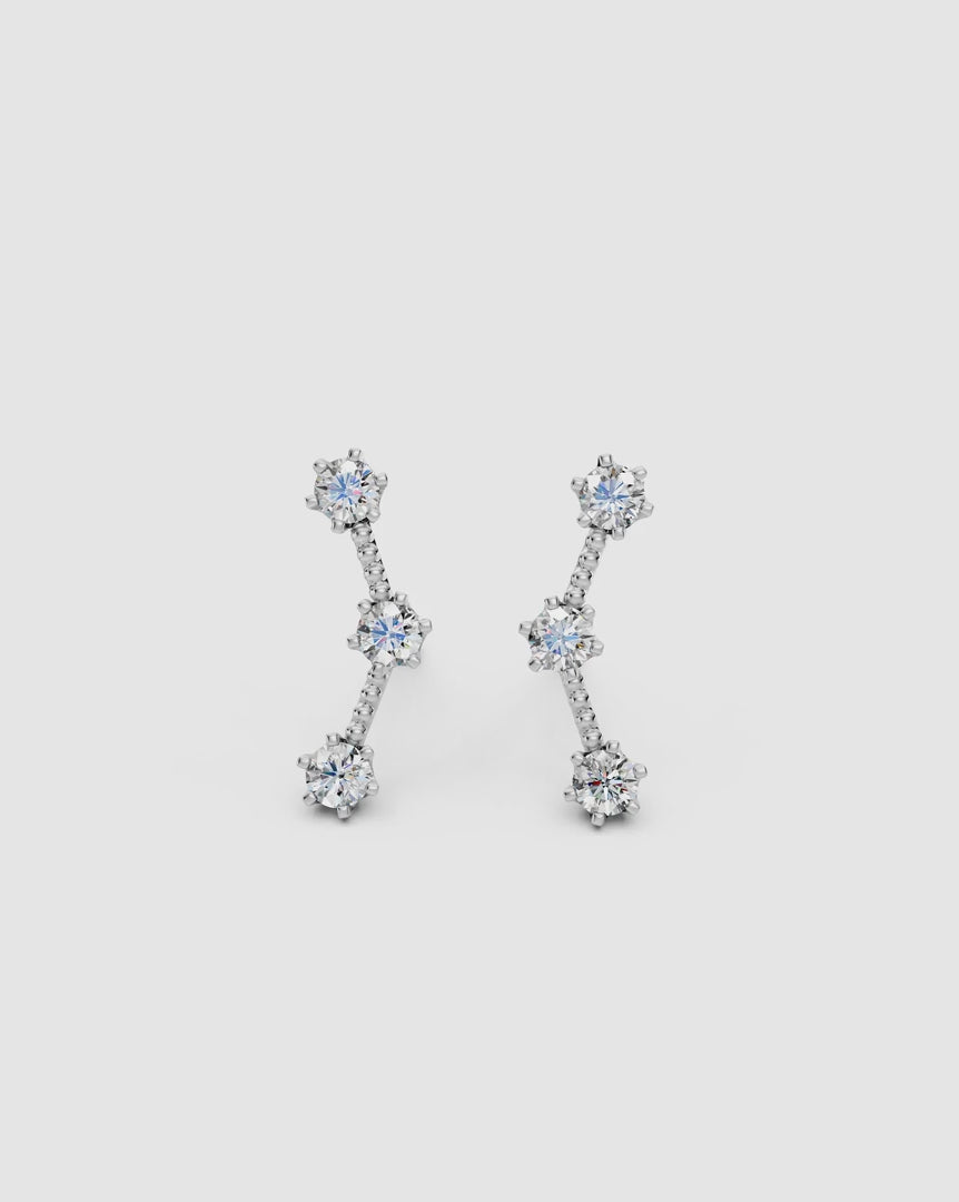 spin video giving 360 view of a pair of 14k white gold celestial climber earrings with three dainty diamonds on an off-white surface