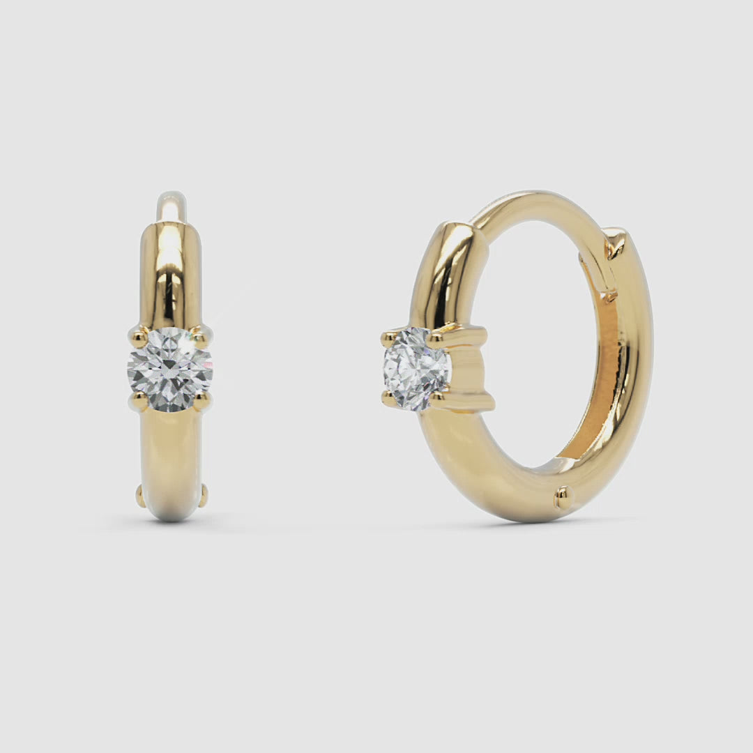 A 360-degree video of 14k yellow gold diamond huggie hoop earrings, smoothly rotating to reveal the polished gold surface and round diamond accent from all angles.
