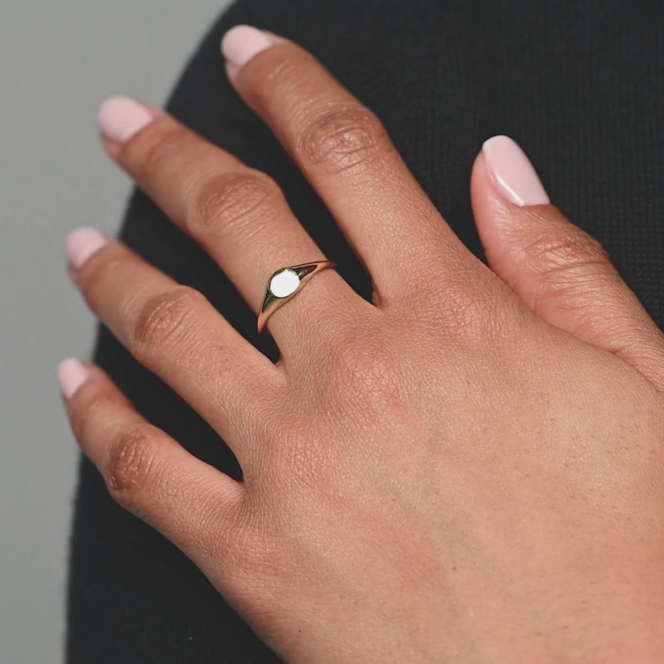 A close-up of a woman’s hand wearing a 14k yellow gold oval signet ring, showcasing its smooth, polished face and elegant simplicity.